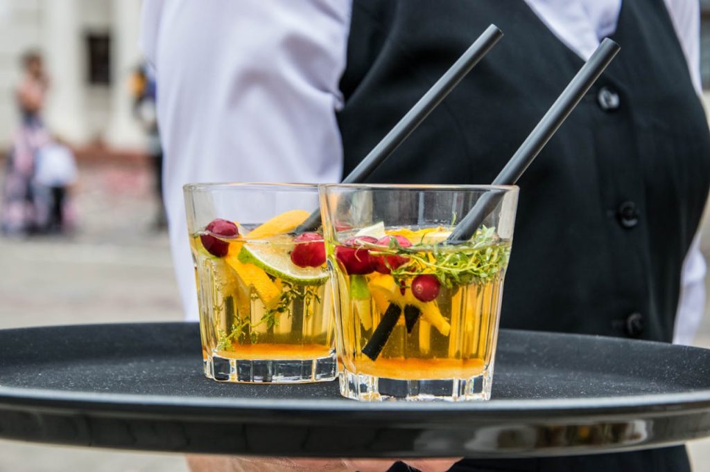 2-whisky-glasses-filled-with-beverage-on-black-tray-169391 Delicious orange cocktails with cranberries and herbs on a tray, served by waiter at an outdoor event.