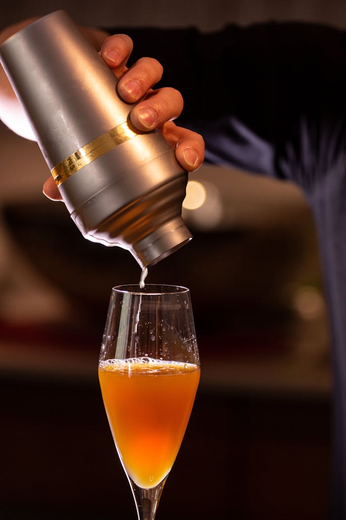Close-up of a vibrant cocktail being poured from a shaker into a cocktail glass indoors.